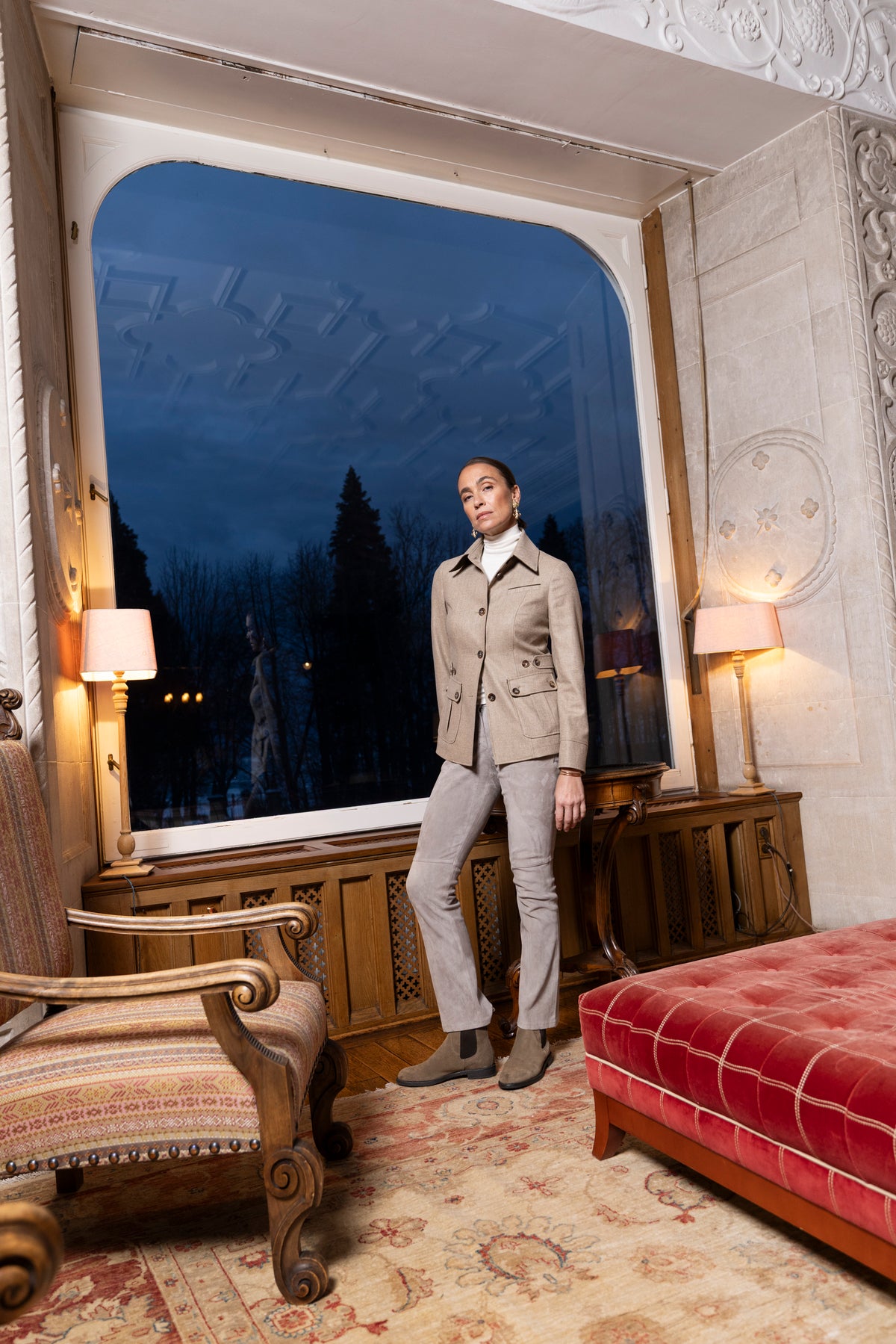 Model in Habsburg Mode posiert vor großem Fenster bei Abenddämmerung